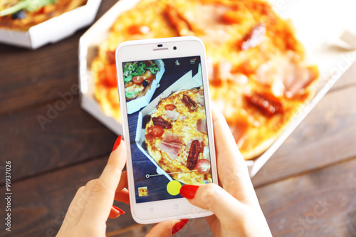 Woman taking a photo of pizza with the smartphone photo