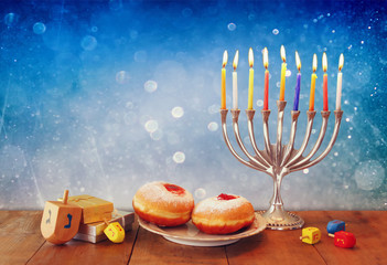 low key image of jewish holiday Hanukkah with menorah, doughnuts and wooden dreidels (spinning top). retro filtered image
