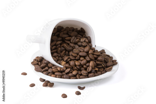 A full cup of roasted coffee beans spilled on a plate.