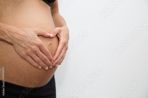 Hände auf dem Bauch einer schwangeren Frau bilden ein Herz