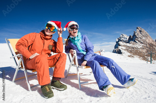 two snowboarders on top of the mountain having fun sitting on