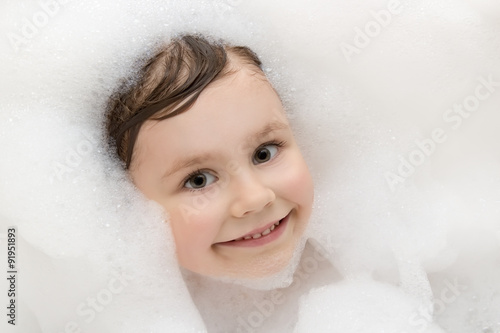 Pretty smiling little girl taking a bath with soap suds