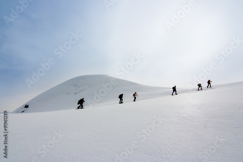 People walking with snow rackets towards the summit of a  hill photo