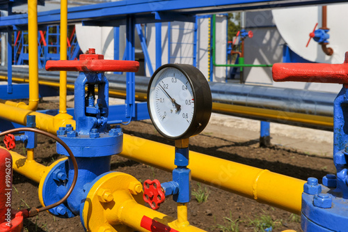 Pressure meter and red faucet with steel yellow pipe in natural gas treatment plant in bright sunny summer day photo