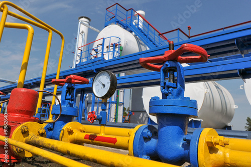 Pressure meter and red faucet with steel yellow pipe in natural gas treatment plant in bright sunny summer day