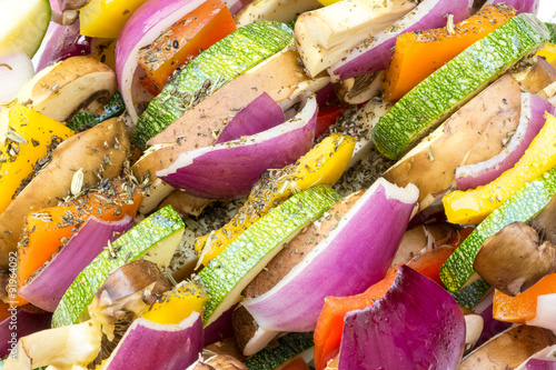 Low calorie bbq sticks with pieces of fresh vegetables as zucchini, mushroom, onion and bell pepper served with olive oil and herbs on a plate ready to grill