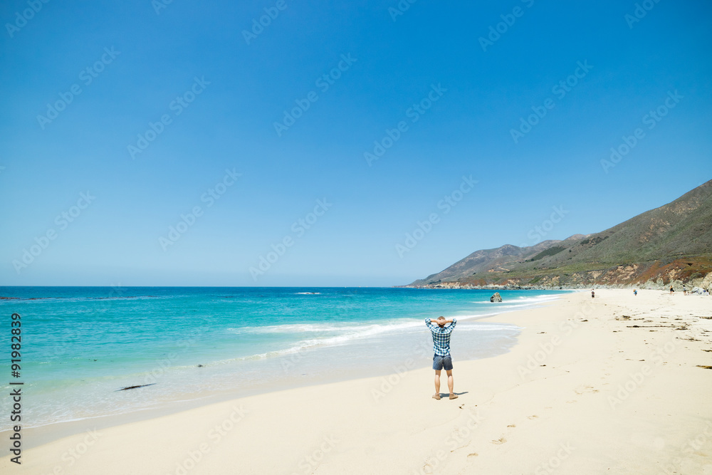 Man relaxing on beautiful white sand beach and clear turquoise water along the Pacific Coast Highway, California, USA