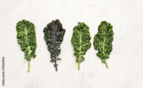 Three leaves of fresh green kale and one of red kale on white table