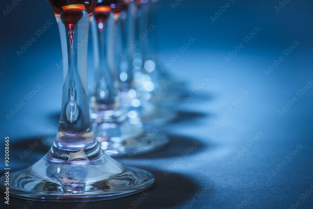 Closeup of aligned wine glasses stems over blue background. Shallow depth of field. Closeup of aligned wine glasses stems over blue background. Shallow depth of field.