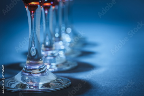 Closeup of aligned wine glasses stems over blue background. Shallow depth of field.