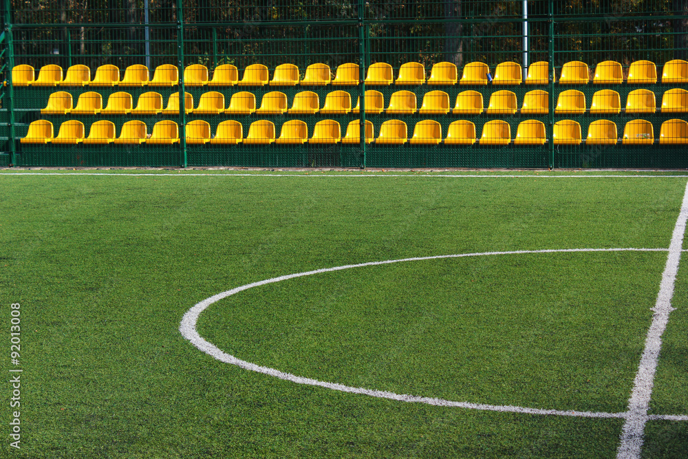 Fototapeta premium Green grass and yellow seats at empty mini soccer stadium