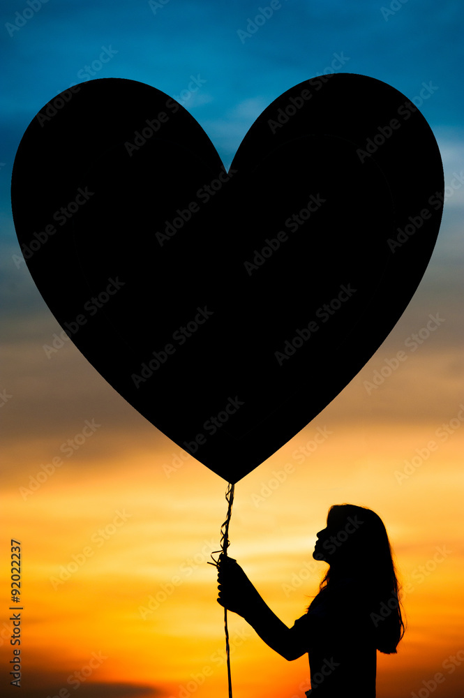 silhouettes of a girl holding heart balloon