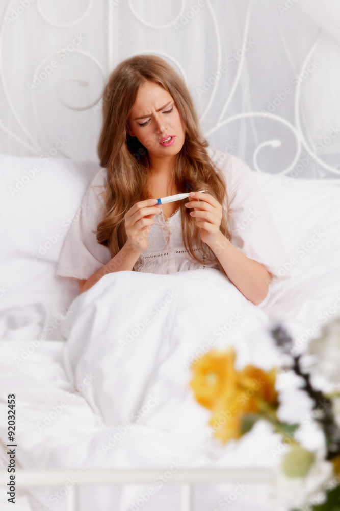 Sick woman in the bed checking the thermometer