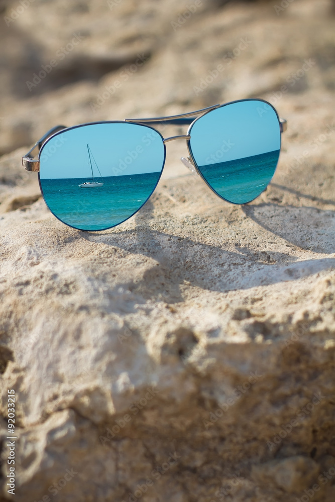 blue mirrored sunglasses on the beach background close up