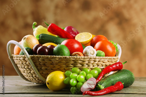 Heap of fresh fruits and vegetables in basket on wooden table close up