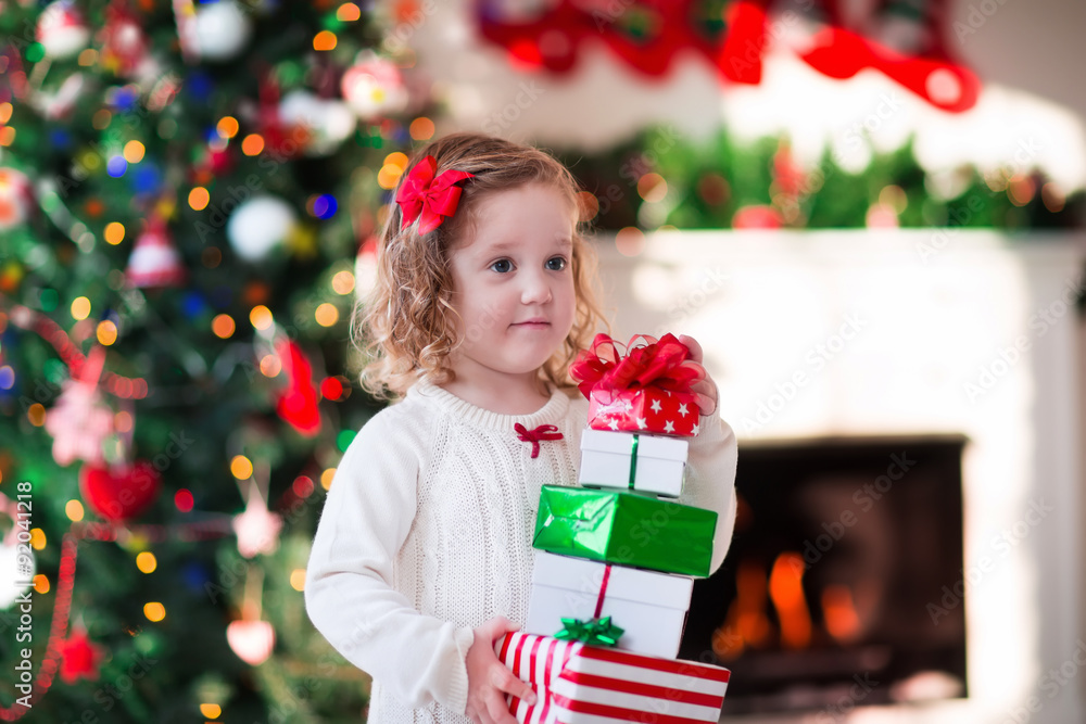 Little girl opening Christmas presents at fire place