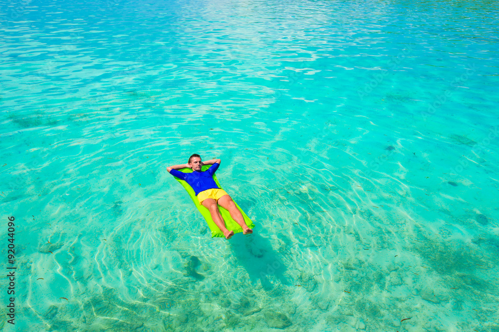 Young happy man relaxing on inflatable mattress in the sea