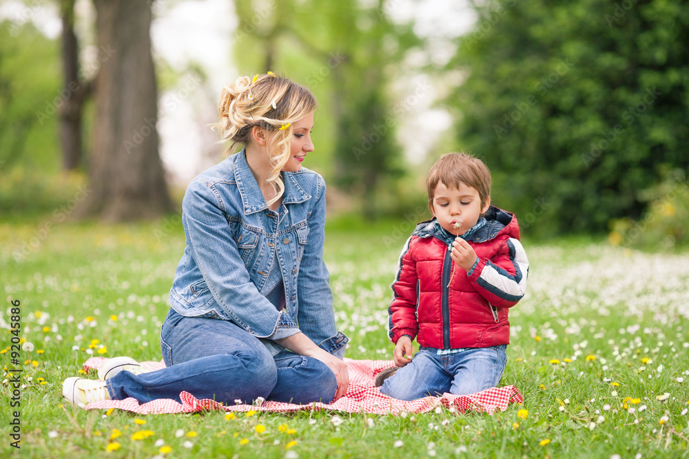 Beautiful family portrait of young mother and her cute son blowing dandelions in nature Beautiful family portrait of young mother and her cute son blowing dandelions in nature