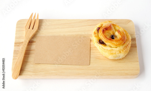 Raisin roll, note paper and fork on wood tray isolated on white