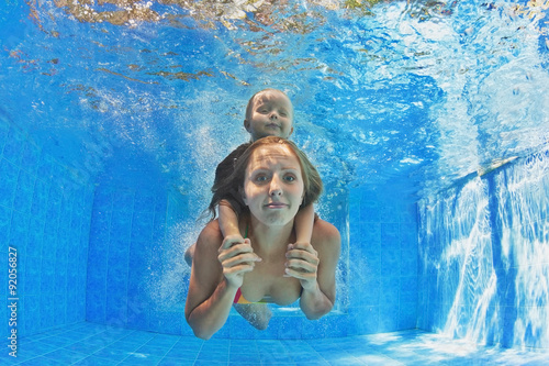 Happy family - mother with baby girl and diving underwater with fun in outdoor pool. Healthy lifestyle, active parents, people water sports activity and swimming lessons on summer holidays with child