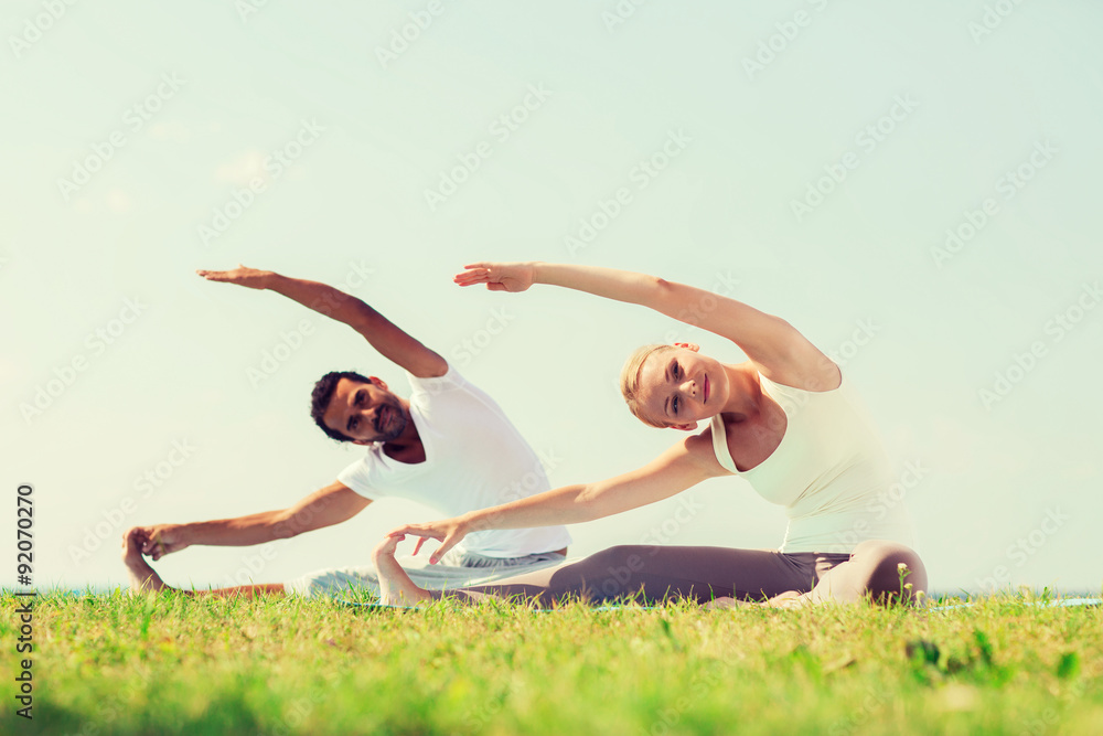 Fototapeta premium smiling couple making yoga exercises outdoors
