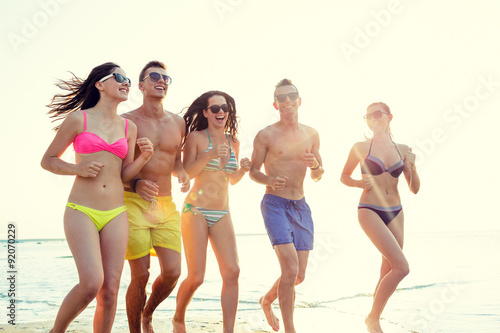 smiling friends in sunglasses running on beach