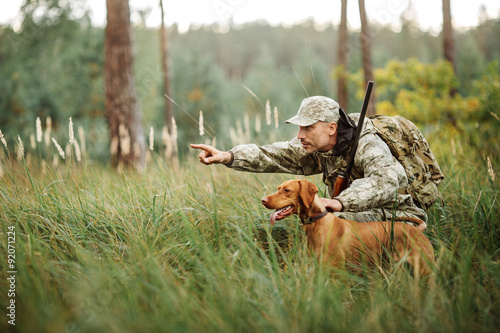 Leinwand Poster Yang Hunter mit Gewehr und Hund im Wald