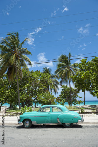 Classic vintage American car stands parked in front of palm trees on the road next to the beach © lazyllama