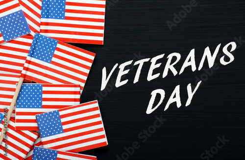 The phrase Veterans Day in white text on a blackboard alongside paper flags of the United States of America