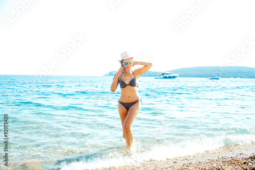 Woman in sun hat and bikini standing with her arm raised to her