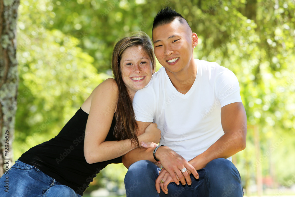 Fototapeta premium Young mixed couple sitting on a bench in a park