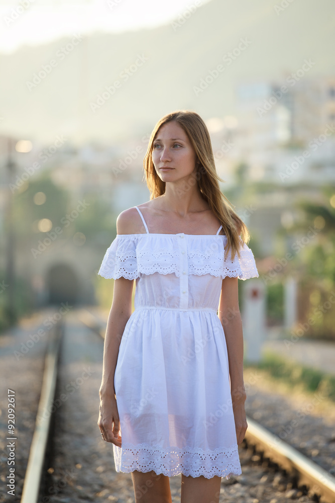 Fototapeta premium Serious young woman in white dress staying in the railwa