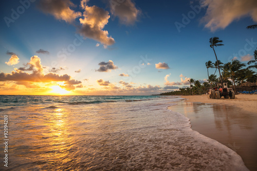 Palm trees sandy beach and cleaning tractor on sunrise