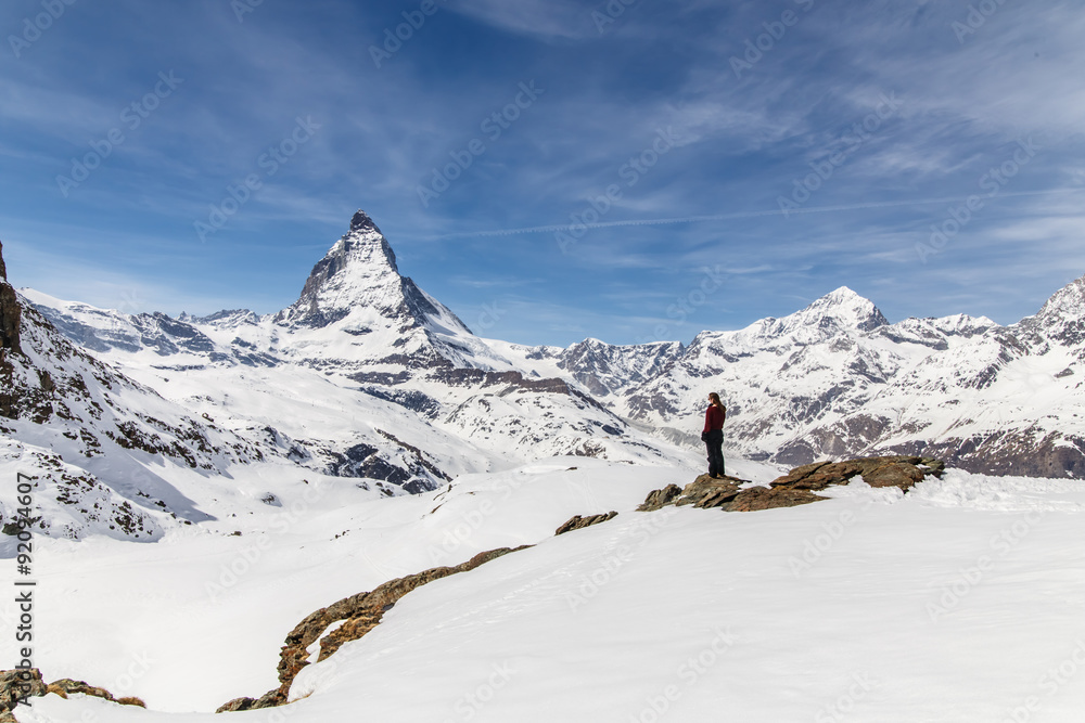 A woman standing on the snow in the background of Matterhorn.