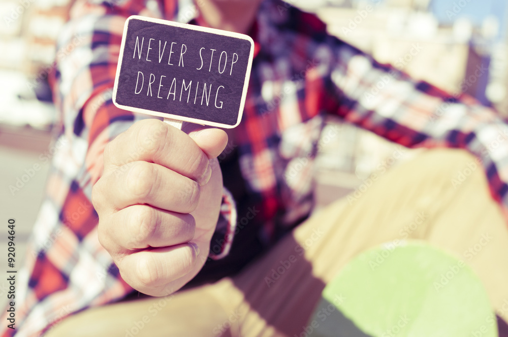 Fototapeta premium young man with a signboard with the text never stop dreaming