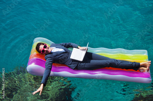 Happy businesswoman with laptop on floating mattress in red sea  