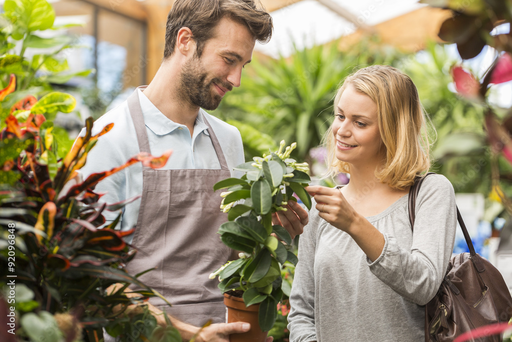Fototapeta premium Male florist serving woman beside display in flower shop, holdin