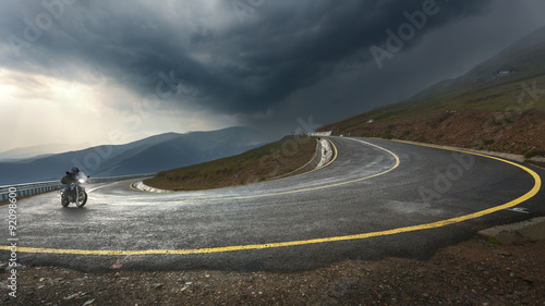 Driving a motorcycle on alpine highway toward the storm