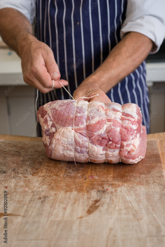 Butcher using string to tie up a joint of raw ham