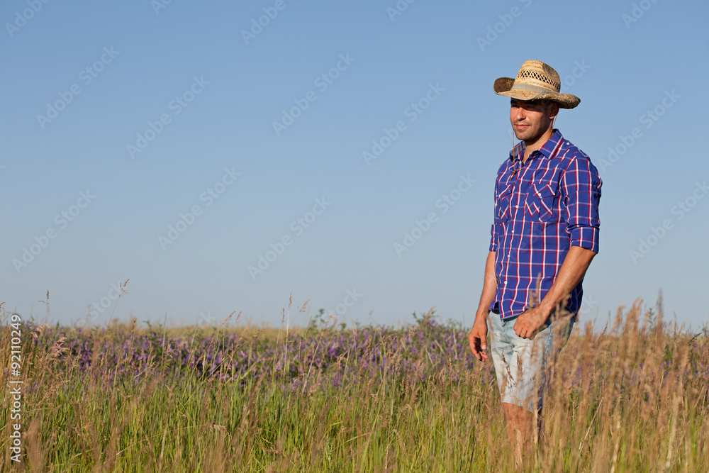 Attractive young man standing in a field. Cowboy