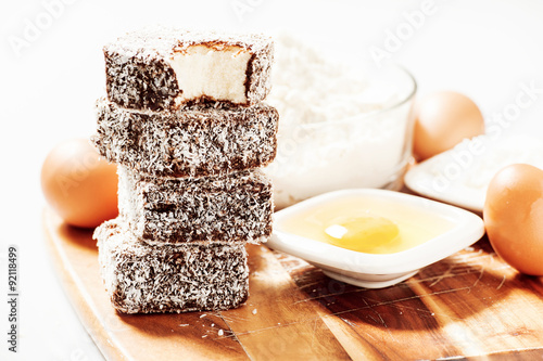 Group of Lamingtons on a timber cutting board with food ingredients in the background 