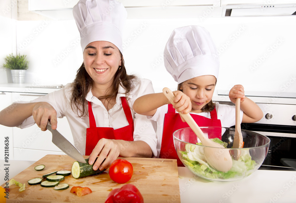 young mother and little daughter at house kitchen preparing salad for lunch wearing apron and cook hat young mother and little daughter at house kitchen preparing salad for lunch wearing apron and cook hat