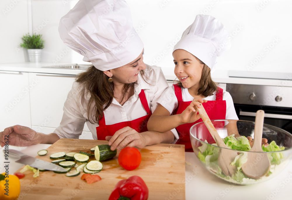 young mother and little daughter at house kitchen preparing salad for lunch wearing apron and cook hat young mother and little daughter at house kitchen preparing salad for lunch wearing apron and cook hat