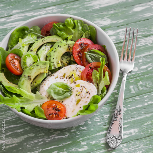 fresh salad with avocado, tomato and mozzarella, in a white bowl on bright wooden surface