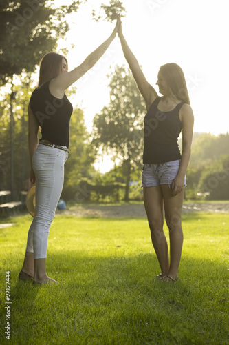 Two girl in strong sunlight, giving high five, using hands.