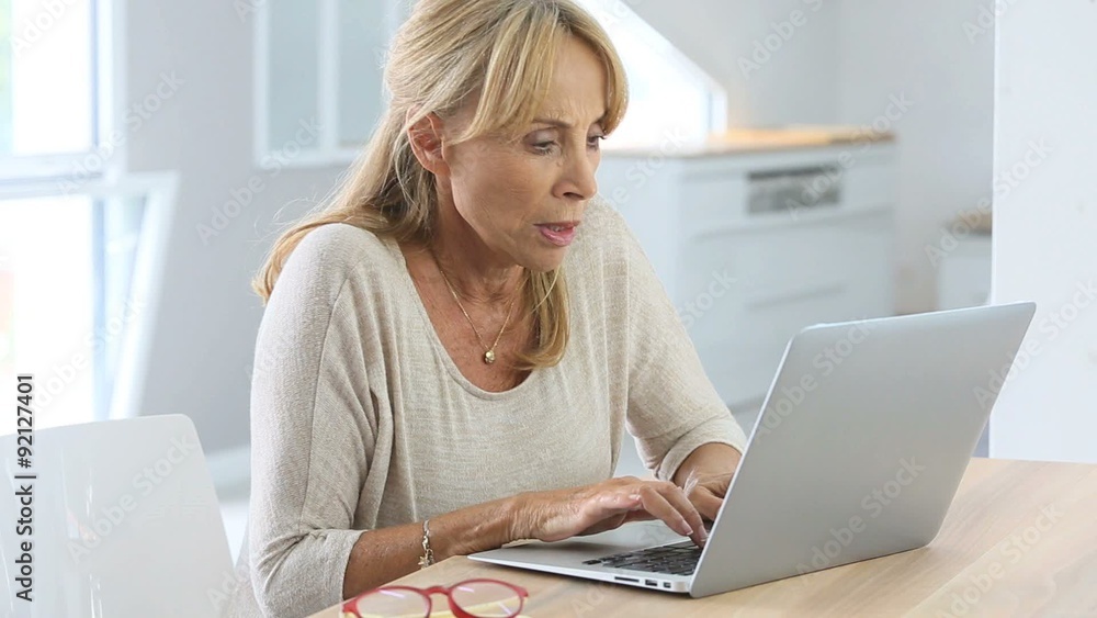 Elderly woman putting eyeglasses on while using laptop Elderly woman putting eyeglasses on while using laptop