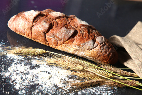 rustic crusty bread and wheat ears on a dark wooden table