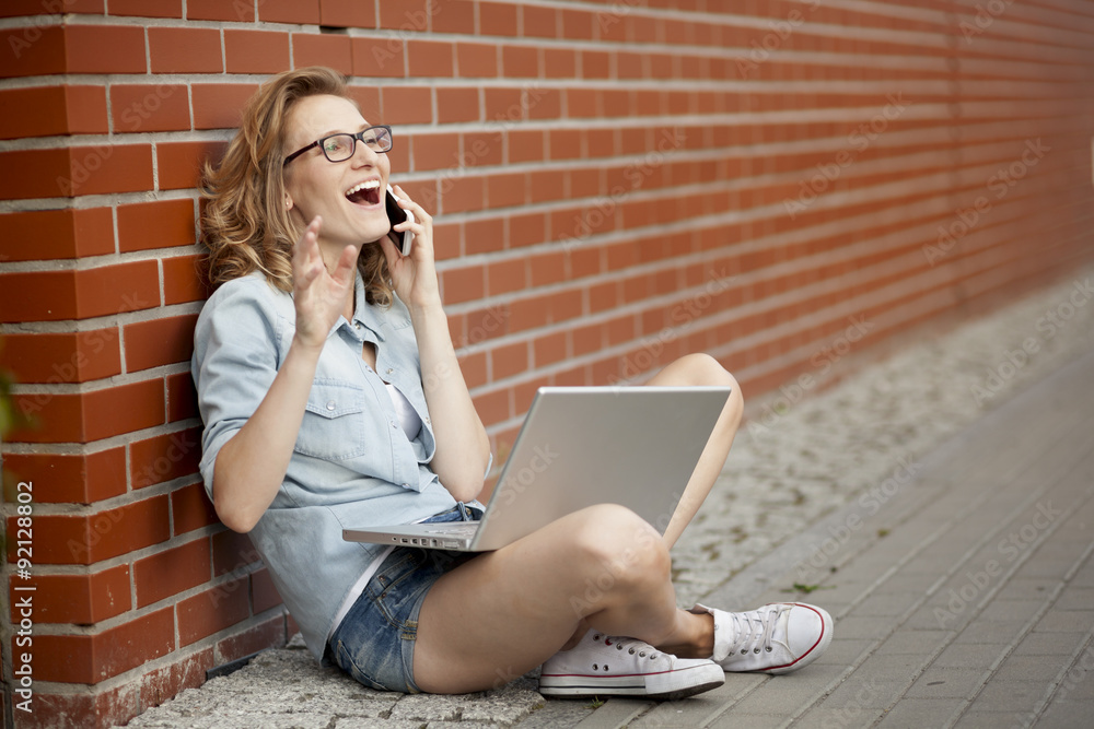 Young student having good time using phone while working outside with laptop Young student having good time using phone while working outside with laptop