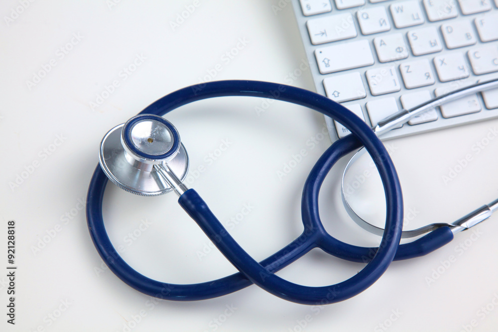 A medical stethoscope near a laptop on a wooden table, on white A medical stethoscope near a laptop on a wooden table, on white