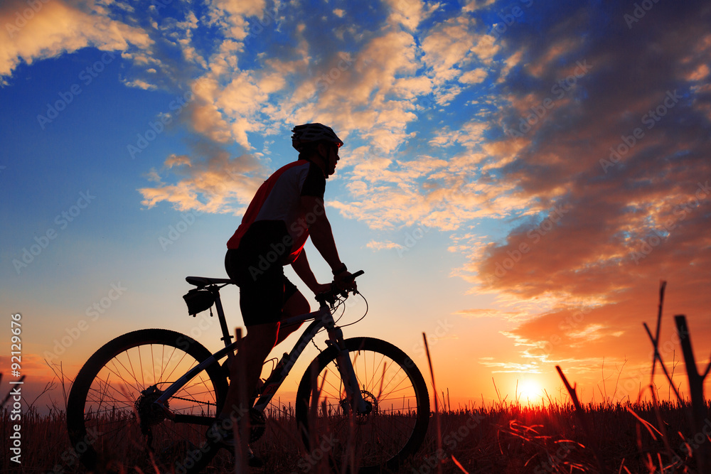 Obraz premium Silhouette of a biker and bicycle on sunset background.
